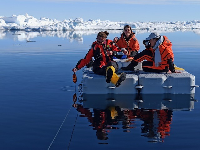 A group of people sitting on a floating platform in large openings between the ice