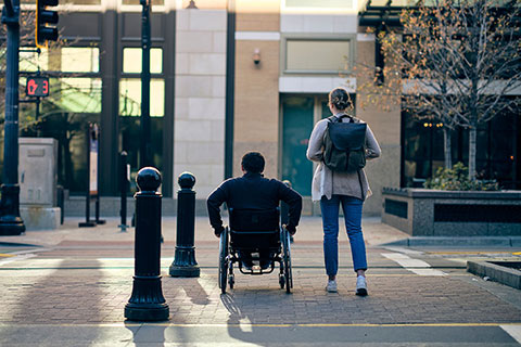 A person sitting in a wheelchair and a standing person at a cross-walk