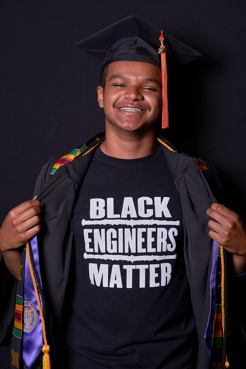 Christopher in graduation cap and gown while revealing a t-shirt underneath that says Black Engineers Matter