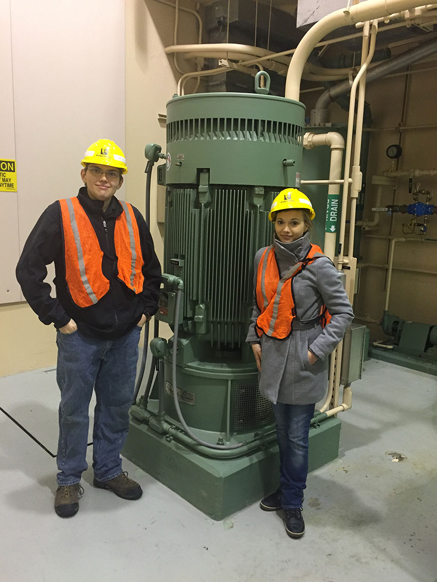 Kat standing with a man in front of machinary wearing hard hat