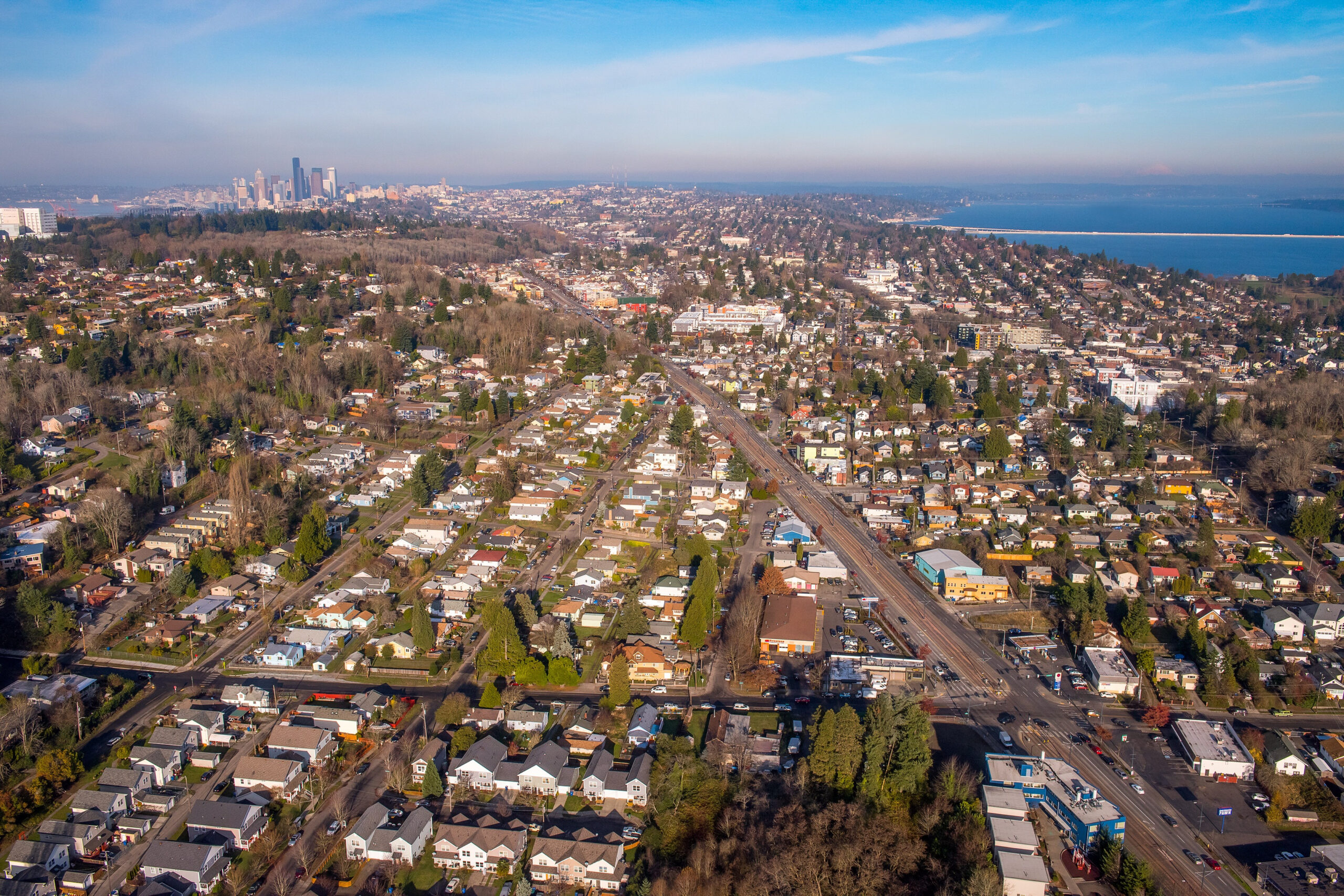 An aerial shot of Seattle showing a large road surrounded by neighborhoods and businesses. There is water on the right and downtown is in the top left.