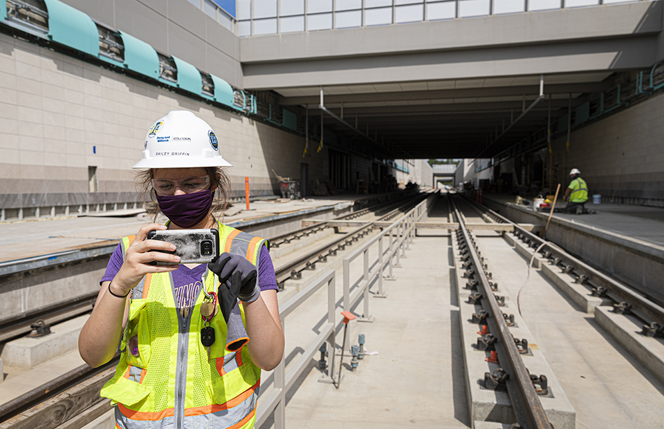 Student taking a photo with her phone next to the train track