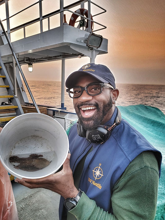 Okereke holding up a bucket that has a turtle inside