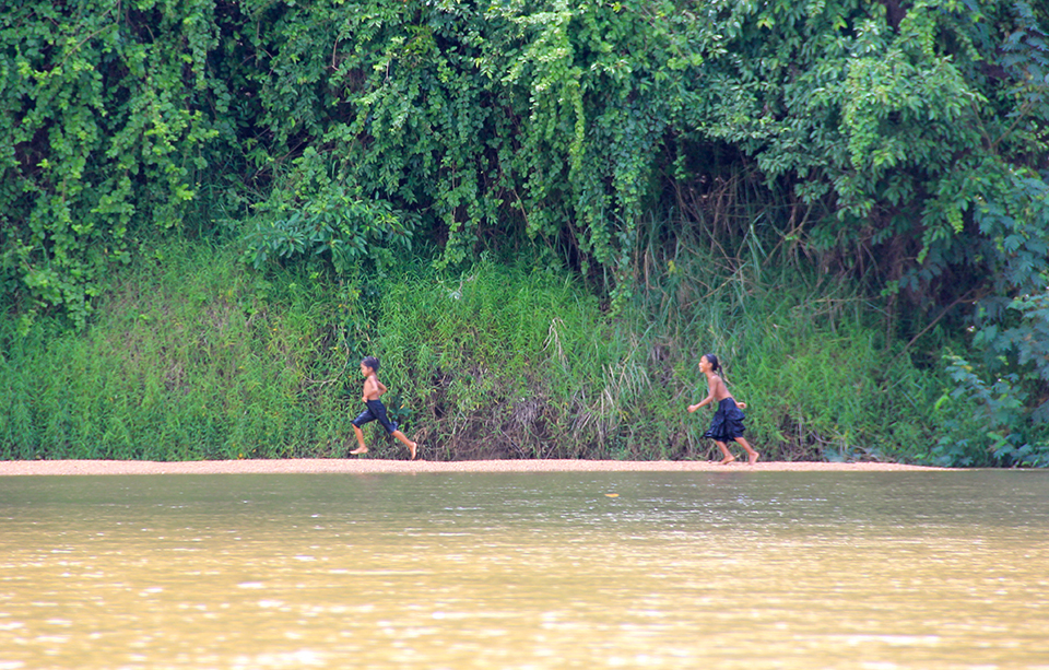 A river in the foreground while children run on the beach in the background