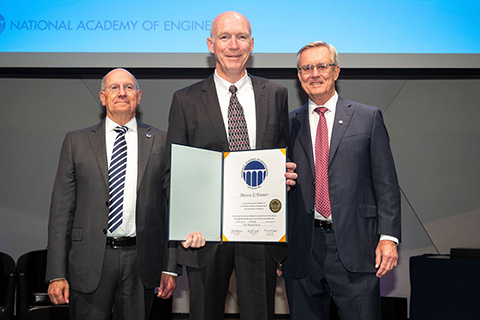 Professor Emeritus Steve Kramer holding a certificate while standing between two NAE officials