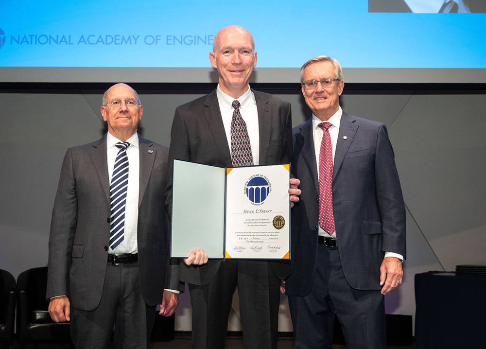 Professor Emeritus Steve Kramer holding a certificate while standing between two NAE officials
