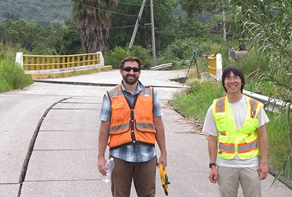 Jake Dafni and Eric Lo stand in front of a damaged roadway