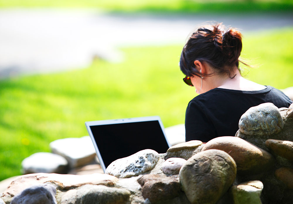A student sitting outdoors in front of a laptop