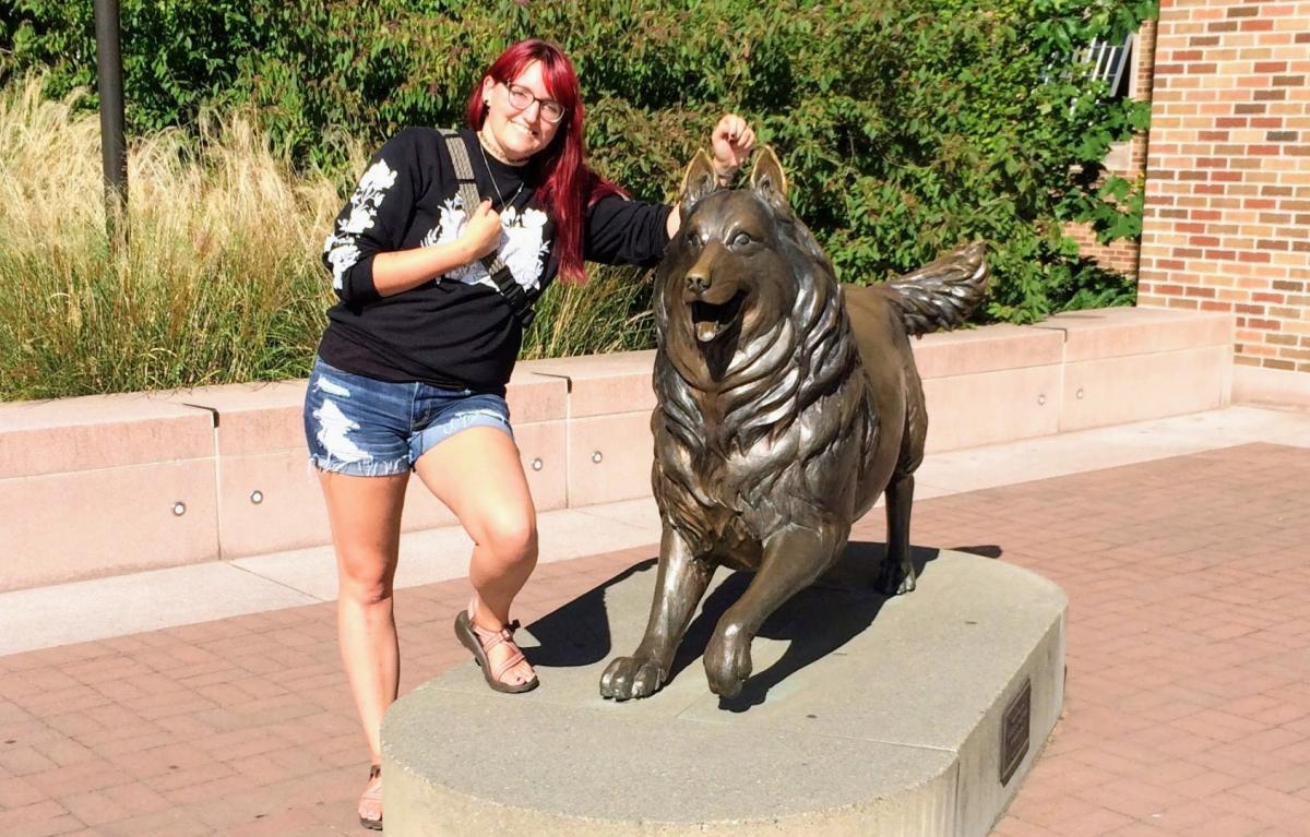 A student posing next to the Husky statue