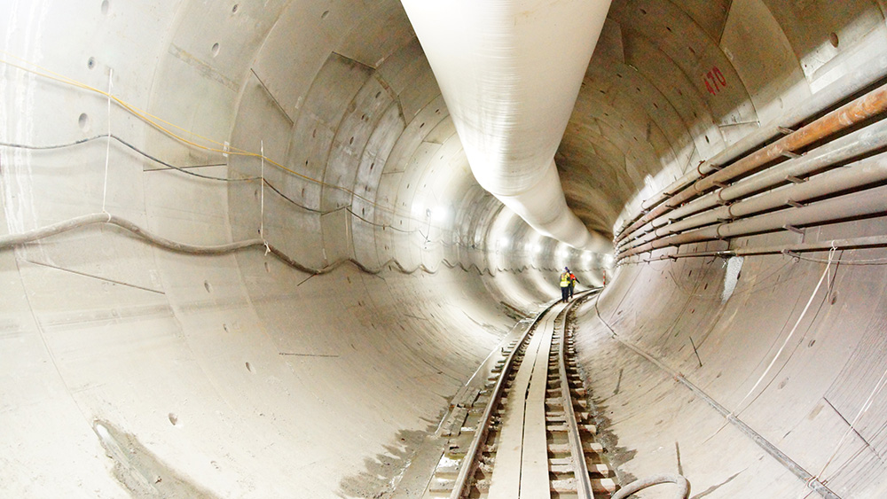 Inside a light rail tunnel with two workers standing on the track