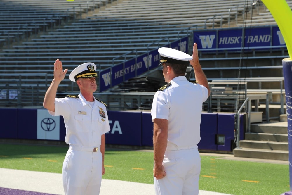 Two military officers in white uniform with their right arm raised at Alaska Airlines Field at Husky Stadium