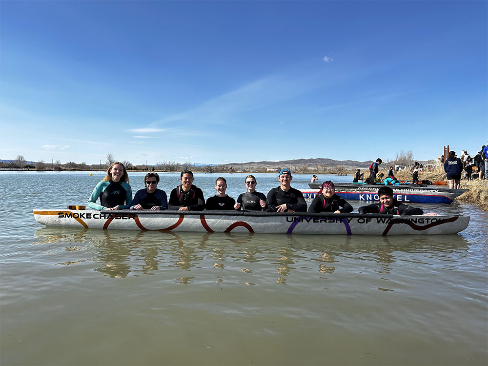 A group of students in a row with their bodies half in the water while holding on to a concrete canoe