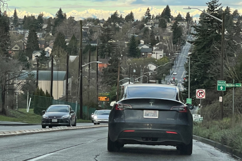 Cars on a road with houses and mountains in the background