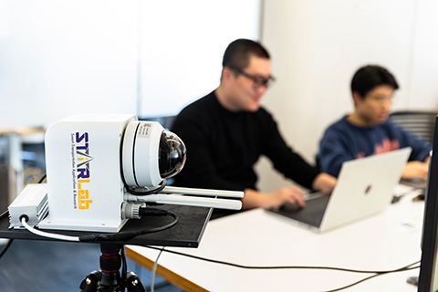 A Mobile Unit for Sensing Traffic (MUST) sensor sitting in the foreground and two researchers working on laptops in the background