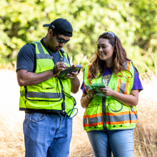 Two students wearing yellow safety vests out doing research in the field