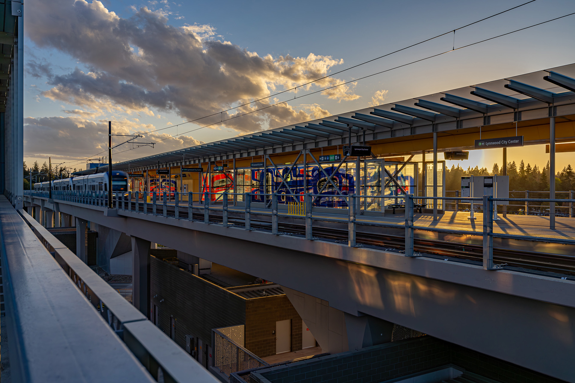 Elevated train station platform at sunset with a moving train
