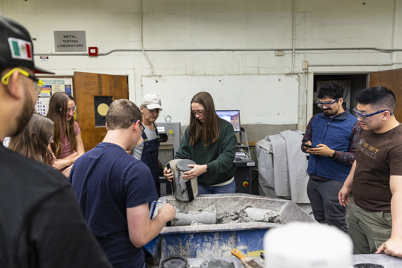 A group of people in a lab handling and examining concrete at a workstation