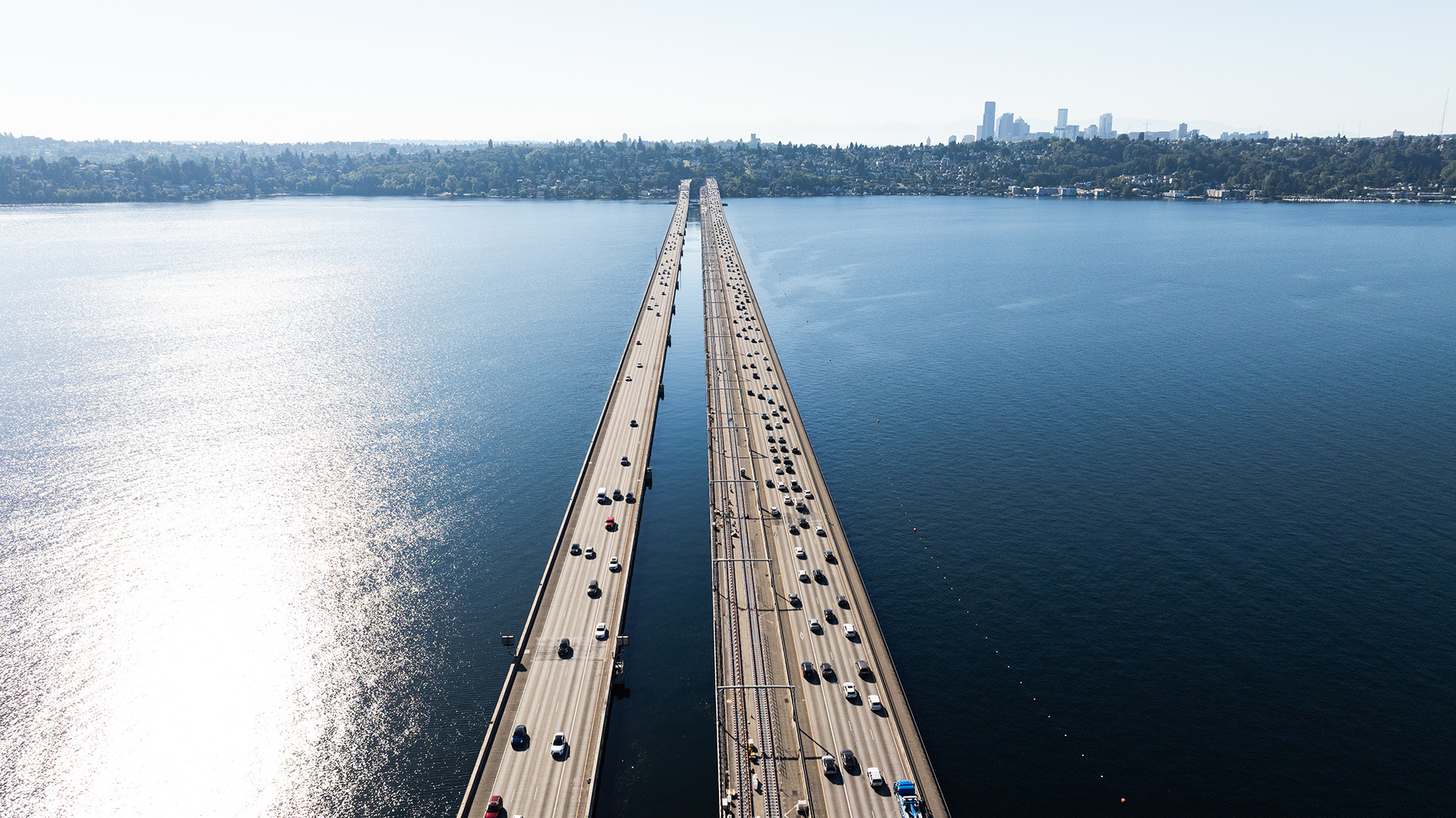 Aerial view of parallel bridges over a large body of water with city skyline in the distance