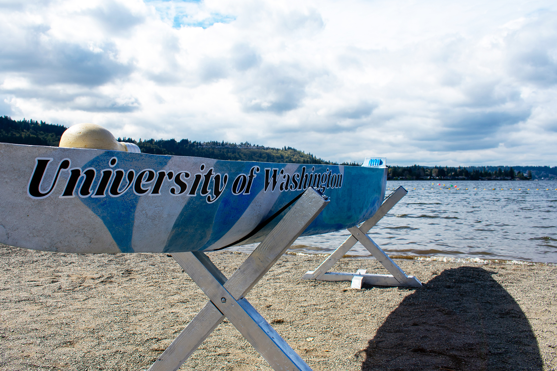 A long blue and white concrete canoe sits on a metal display stand, with “University of Washington” painted along its side