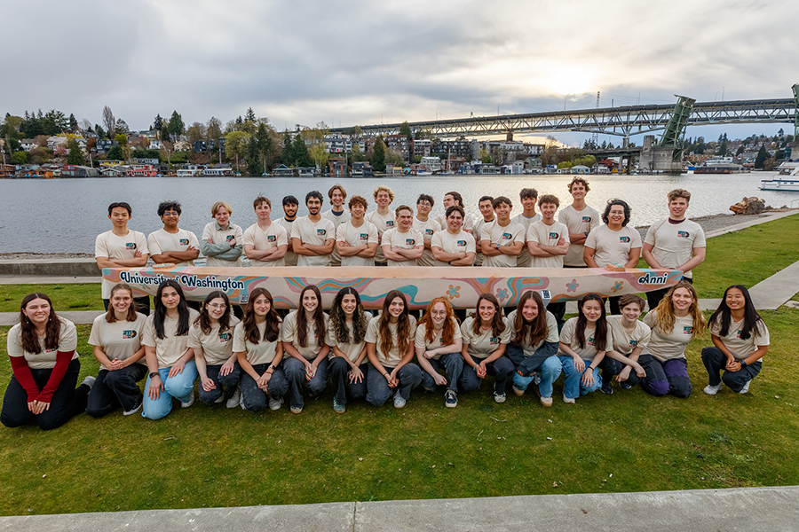 The 2025 UW Concrete Canoe Team poses on the waterfront with their canoe, Anni, which features colorful 1970s-inspired artwork.