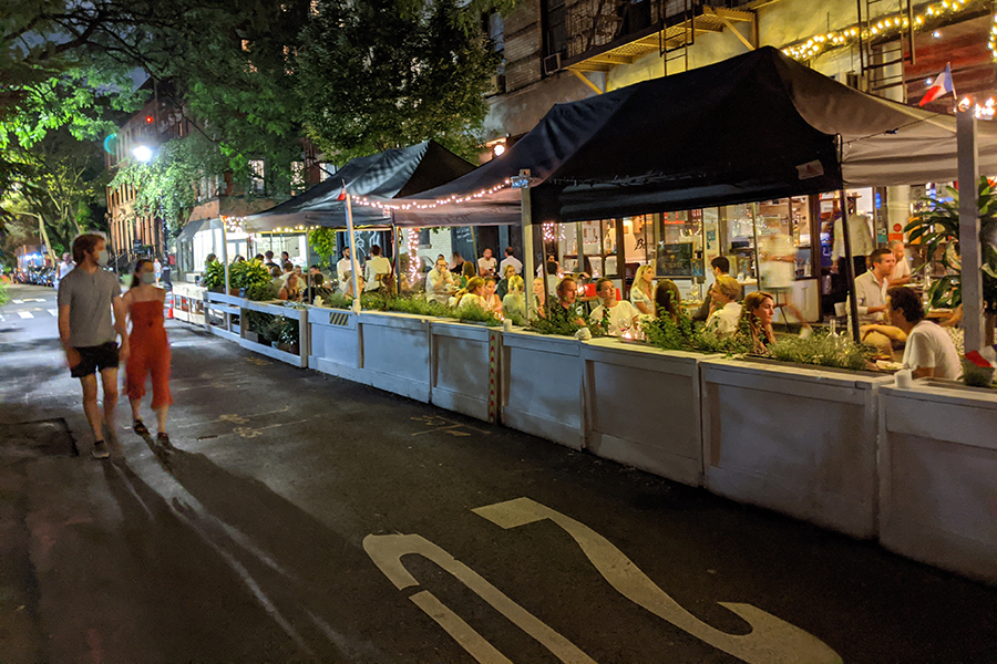 A couple walks down the street past a restaurant using the street as outdoor dining.