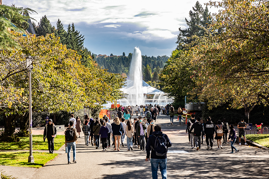 Students walk down an outdoor path towards a fountain on the University of Washington campus.
