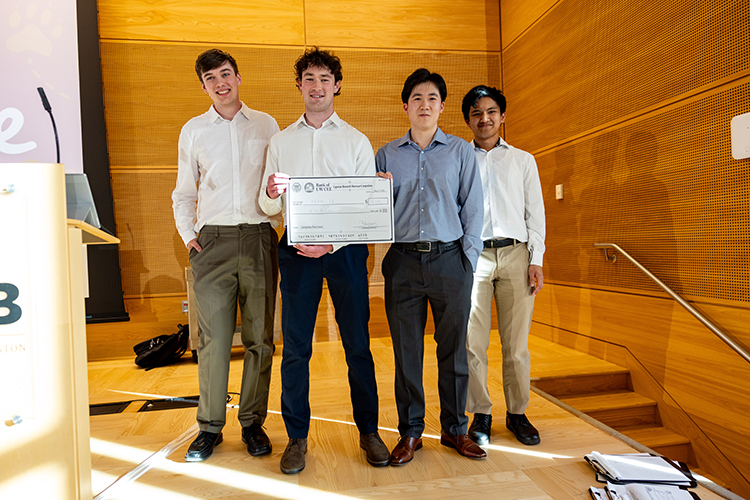 Four students stand on stage holding a large novelty award check. 