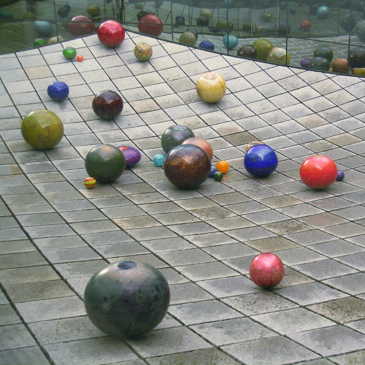 Colorful glass spheres of various sizes scattered across a large undulating stone surface made of square-cut tiles.