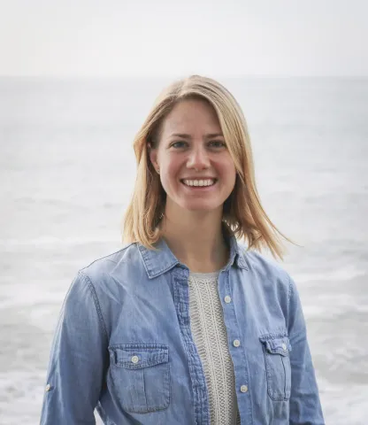 Christie Hegermiller stands on a beach with the ocean behind her.