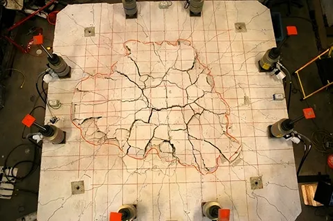Top view of a slab after a punching shear test, showing cracks radiating outward from the center, where the column supported the slab from below.