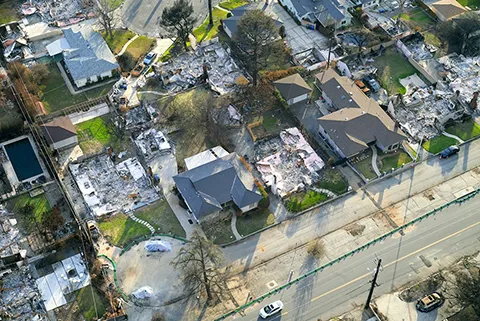 An aerial view of a neighborhood where some homes have been completely destroyed by wildfires while other homes are left untouched.