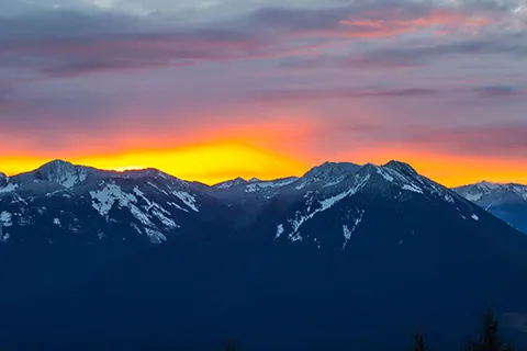 A mountain range with the sun setting behind the mountains.