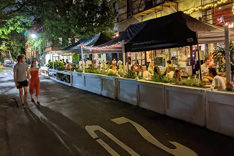 People walk down the street past a restaurant using part of the street for outdoor dining.
