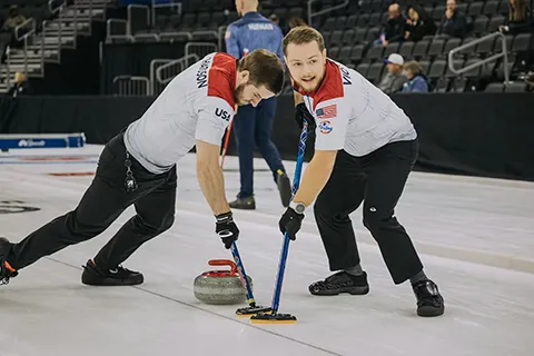 Two men curling on ice.