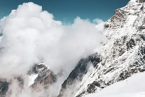 Clouds of snow rush down a steep mountainside.