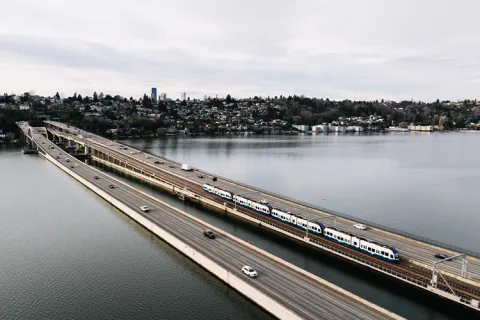 Aerial view of a bridge with a light rail train and cars over a body of water.