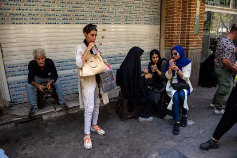 Women in Iran waiting at a bus stop while drinking cool drinks during a heat wave.