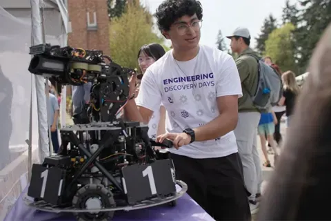 A student in a white shirt showing a robot on display.