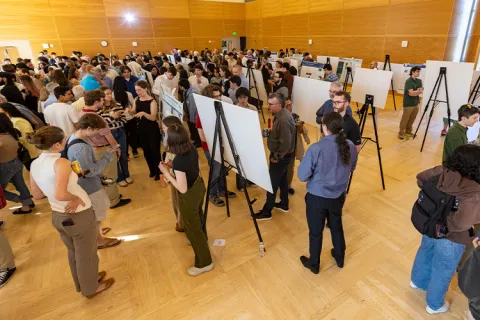 A large crowd mingles among rows of poster easels in a event hall. 
