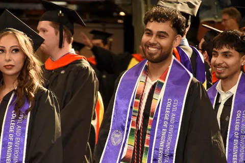A student wearing a sash that says "Civil & Environmental Engineering" smiles during graduation. 