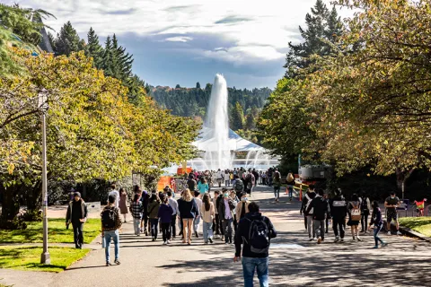 Students walk on an outdoor pathway with a fountain in the background on the UW campus.
